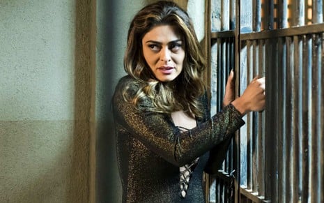 A atriz Juliana Paes com expressão séria e roupa de festa numa cela de cadeia em cena de A Força do Querer