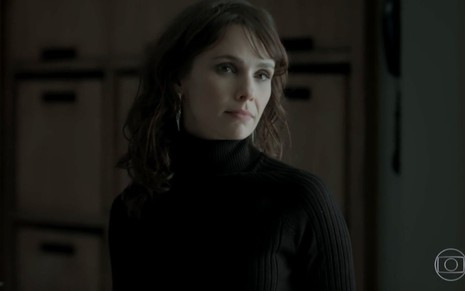 A atriz Débora Falabella com expressão séria, de blusa preta em frente a fundo escuro, em cena de A Força do Querer