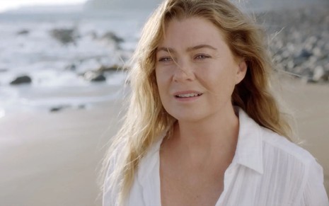 Ellen Pompeo, vestida de branco, está em uma praia com expressão de choque em cena de Grey's Anatomy
