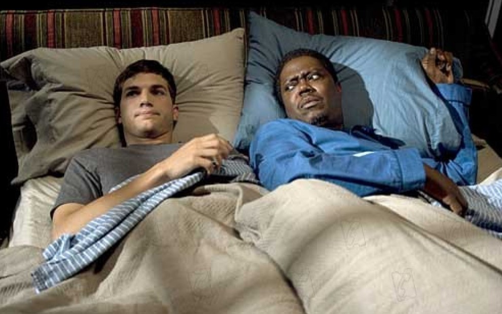 Ashton Kutcher deitado na cama, enquanto Bernie Mac está deitado ao seu lado olhando para ele