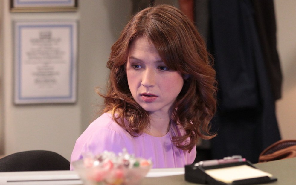 Erin Hannon (Ellie Kemper) em cena de The Office de blusa rosa atrás de uma mesa de escritório