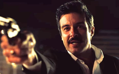 Gustavo Vaz aponta uma arma de fogo com expressão de ódio em cena como o personagem Augusto de Coisa Mais Linda