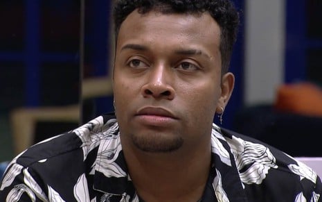 Nego Di no Big Brother Brasil 21: com camiseta florida, participante olha de maneira séria para alguém fora do quadro