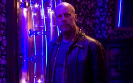 Em um ambiente com luz azulada, Bruce Willis está olhando para frente em cena do filme Substitutos (2009)