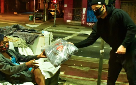 O ator Felipe Titto distribuindo cobertor a mulher em situação de rua na noite de sábado (30), em São Paulo
