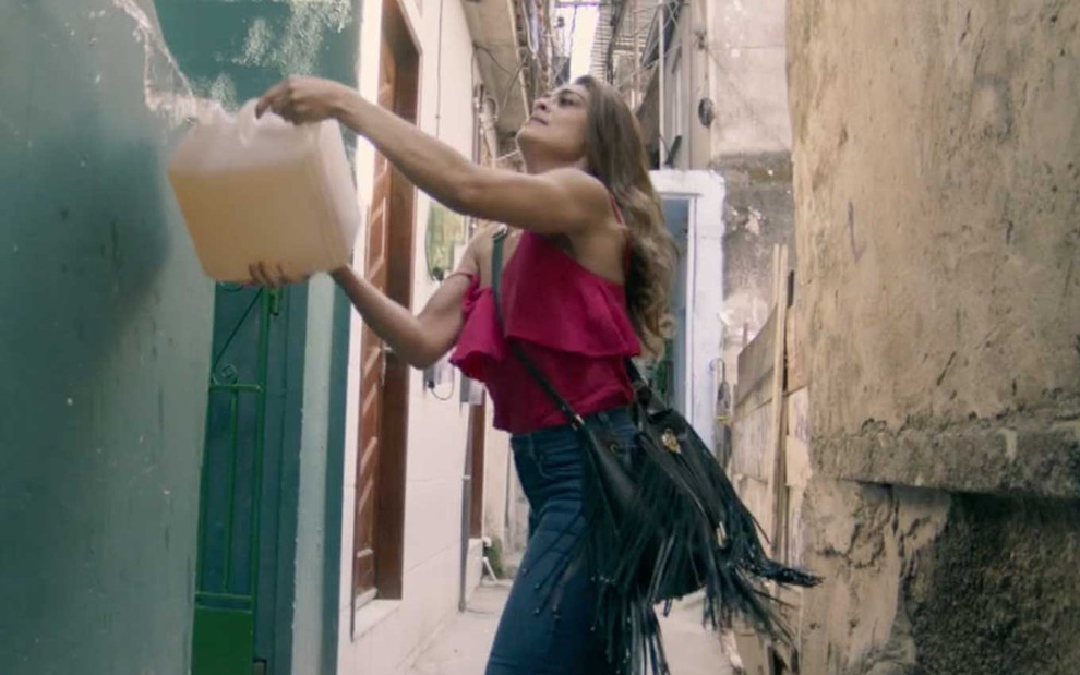 Juliana Paes caracterizada como Bibi em A Força do Querer: personagem segura um galão de gasolina e joga o líquido em porta de uma casa