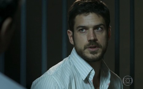 O ator Marco Pigossi em uma cela, usando uma camisa branca, como Zeca em A Força do Querer