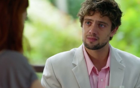 O ator Rafael Cardoso está com um blazer cinza e uma camisa cor de rosa e com expressão de choro como Rodrigo em cena de A Vida da Gente