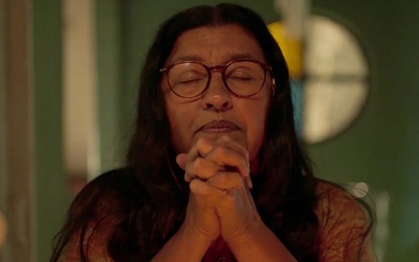 Regina Casé em cena de Amor de Mãe: caracterizada como Lurdes, personagem está de olhos fechados e ora