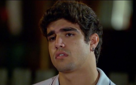 O ator Caio Castro caracterizado como Antenor usa camiseta polo cinza e tem olhar desconfiado em cena de Fina Estampa