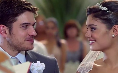 Marco Pigossi usa terno e olha sorrindo para Sophie Charlotte, que está vestida de noiva em cena de Fina Estampa