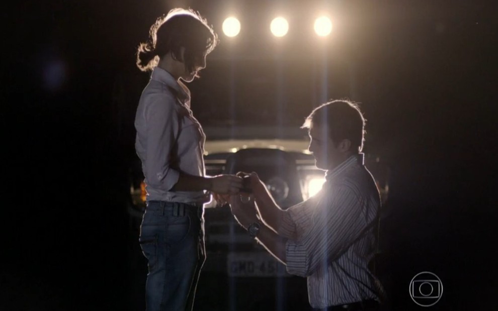 Os atores Tainá Müller e Max Fercondini nos papéis de Ciro e Mila na novela Flor do Caribe; ele está ajoelhado diante dela e colocando um anel em sua mão