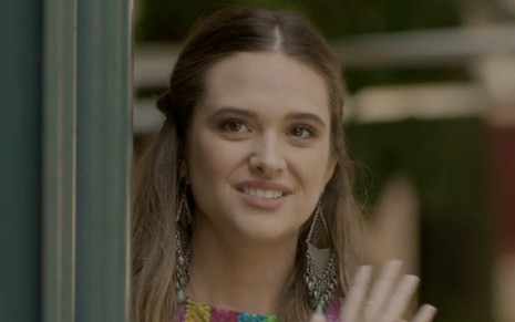 Juliana Paiva caracterizada como Cassandra em Totalmente Demais: a loira tem olhar arrependido e acena para alguém