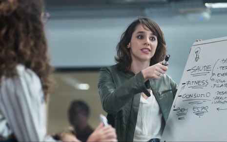A atriz Manoela Aliperti como Lica segura um pincela atômico na frente de um quadro branco em cena de As Five