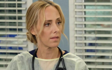 Com um estetoscópio pendurado no pescoço e cabelo preso, Kim Raver aparece em cena da 16ª temporada de Grey's Anatomy