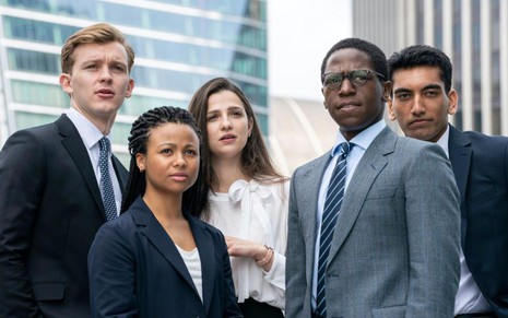 Cinco atores caracterizados com roupas sociais, em foto de divulgação da série Industry, da HBO, com prédios espelhados ao fundo