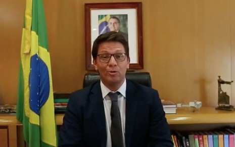 O secretário da Cultura do governo federal Mario Frias sentado em sua mesa como uma foto do presidente Jair Bolsonaro ao fundo