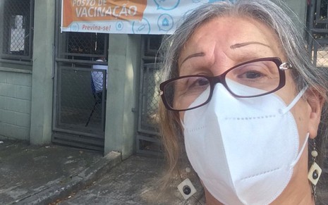 Laerte Coutinho, de máscara e óculos, em frente a entrada da UBS São remo com faixa indicando "Aqui: posto de vacinação"
