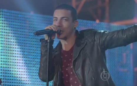 O cantor Di Ferrero de braços abertos num palco, segura microfone em cena de show em Malhação