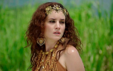 A atriz Elisa Pinheiro em um prado verdejante como Ayla, ela faz a menção de virar a cabeça para trás em cena de Gênesis