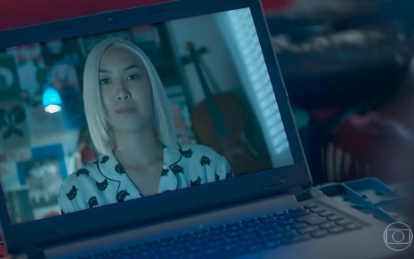 Tina (Ana Hikari) com o cabelo loiro em uma chamada de vídeo em cena de Malhação