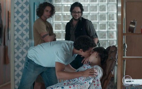 Deco (Pablo Morais) e Roney (Lucio Mauro Filho) em pé veem Tato (Matheus Abreu) beijar o rosto de Keyla (Gabriela Medvedovski), que está dormindo em uma poltrona