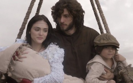 Anna (Isabelle Drummond) e Joaquim (Chay Suede) dentro de um balão com um bebê e uma criança em cena de Novo Mundo