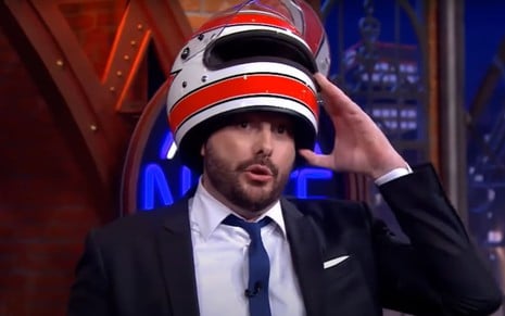 O apresentador Danilo Gentili segura um capacete em cima de sua cabeça durante o programa The Noite, do SBT, exibido na noite de segunda-feira (26)
