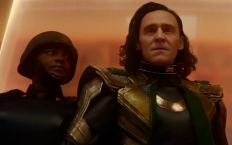 Loki (Tom Hiddleston) no lado direito sendo preso por uma guarda de roupa preta no lado esquerdo em cena da série Loki