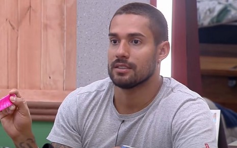 Bil Araújo está de camiseta cinza e conversando na sede de A Fazenda 13, da Record