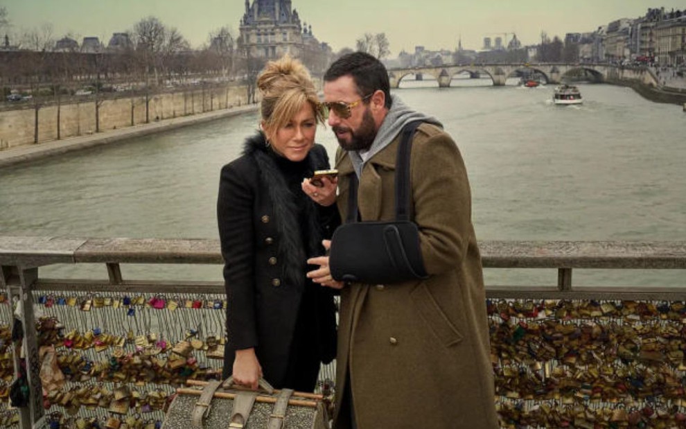 Jennifer Aniston e Adam Sandler em cima de uma ponte em Paris, segurando um celular e uma mala