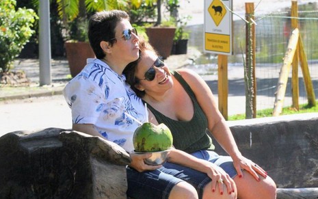 Imagem de Adriane Bonato (à esq.) e Claudia Rodrigues sentadas e abraçadas em uma praça