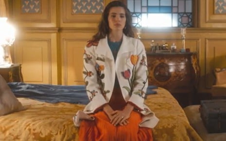A atriz Camila Queiroz sentada numa cama, com roupa de festa e expressão triste em cena de Amor Perfeito