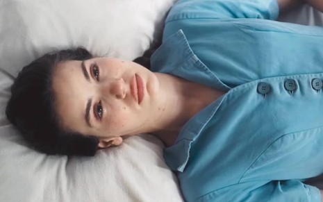 A atriz Camila Queiroz deitada, com expressão triste, em cena de Amor Perfeito