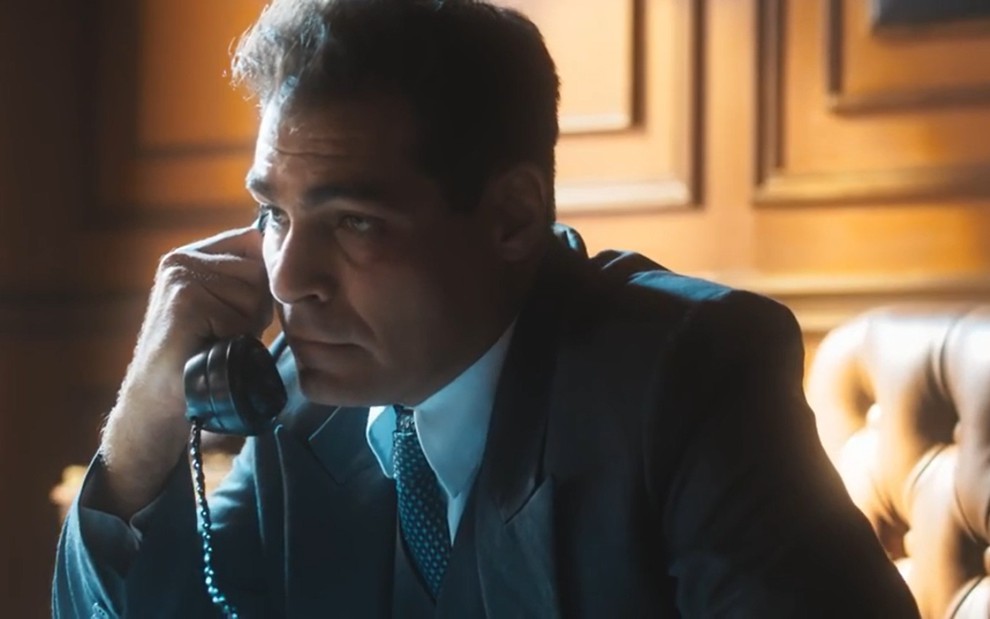 O ator Thiago Lacerda falando ao telefone, de terno e gravata, em cena de Amor Perfeito