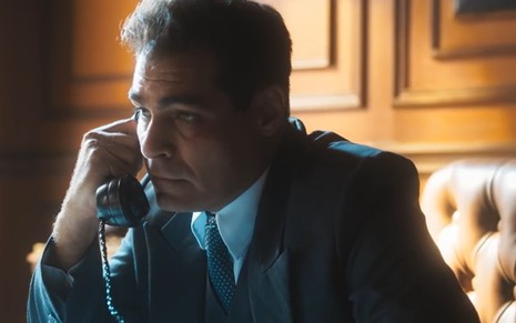 O ator Thiago Lacerda falando ao telefone, de terno e gravata, em cena de Amor Perfeito