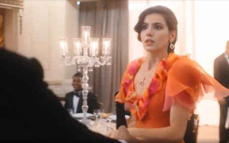A atriz Camila Queiroz de vestido laranja de festa e expressão assustada em Amor Perfeito