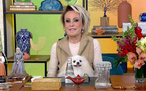 Ana Maria Braga segurando a cachorra Paçoca no colo, sentada no cenário do programa Mais Você
