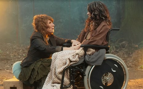Em cena de Vai na Fé, Renata Sorrah está abaixada no pé da cadeira de rodas de Claudia Ohana