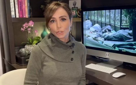 Elaine Bast fala durante uma reportagem da Globo; ela veste blusa de tricô com botões laterais na gola