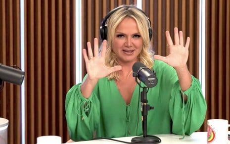 A apresentadora Eliana diante de um microfone, com um fone no ouvido, mostra os dez dedos em um estúdio