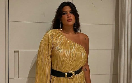 Giulia Costa posa com vestido dourado com o ombro esquerdo à mostra