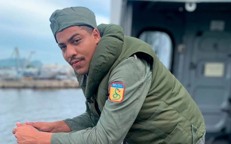 Matheus Dias, caracterizada como Bento, veste uniforme da FEB e se apoia na borda de um navio; ele encara a câmera com um meio sorriso em registro nos bastidores de Além da Ilusão