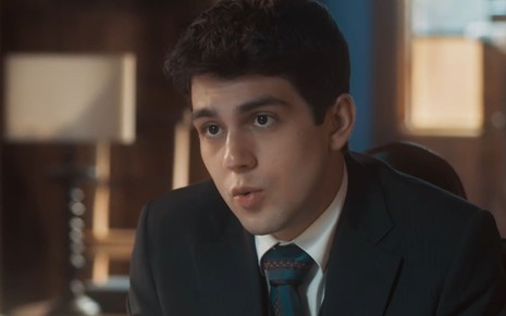 Daniel Rangel caracterizado como Júlio; ele usa um terno azulado e está sério em cena de Amor Perfeito