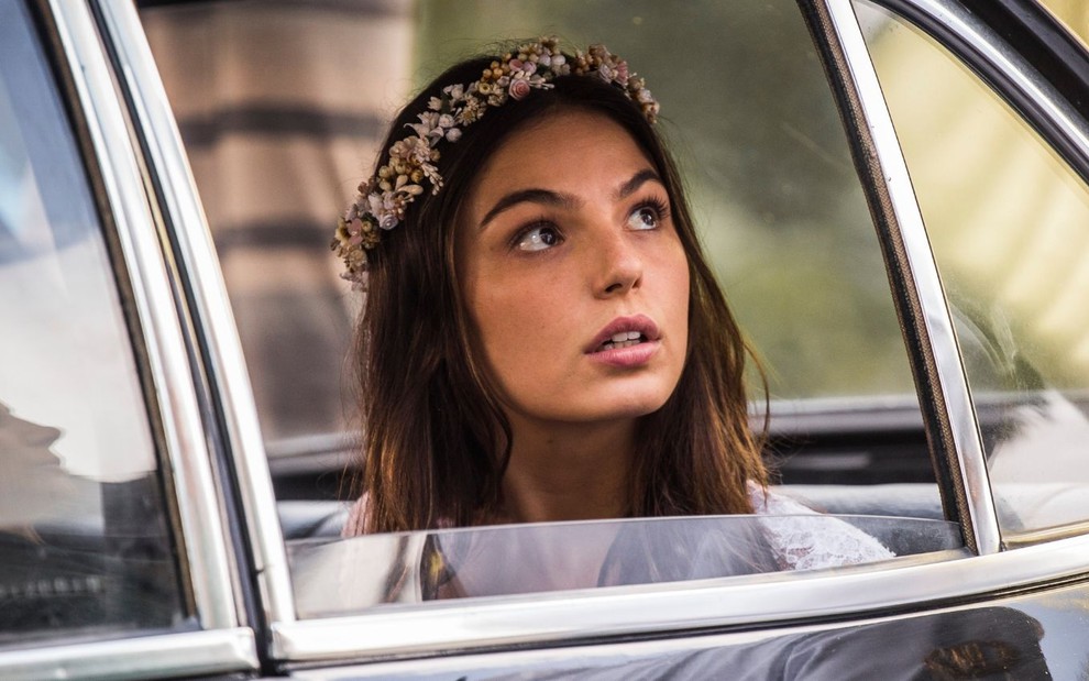 Isis Valverde como Sandra em Boogie Oogie: atriz usa coroa de flores, está sentada no carro e olha para alguém pela janela