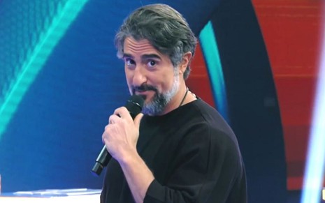 O apresentador Marcos Mion sorri segurando um microfone no programa Caldeirão, da Globo