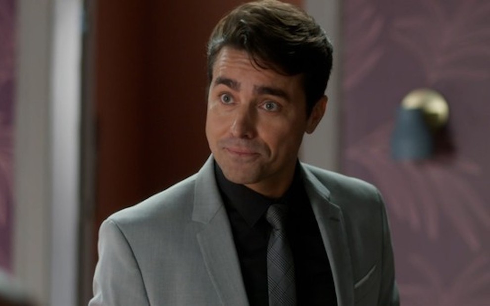O ator Ricardo Pereira usa camisa preta e terno e gravata cinza em cena de Cara e Coragem, novela na qual interpreta Danilo