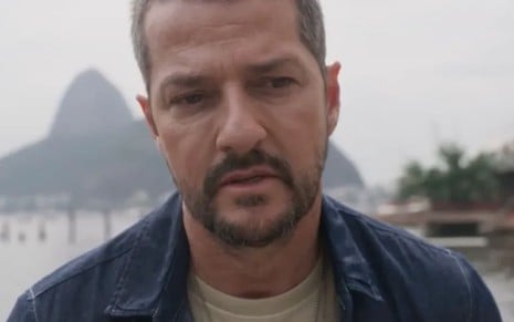 Marcelo Serrado usa uma camiseta e uma jaqueta gasta; ele tem a expressão perturbada em cena de Cara e Coragem