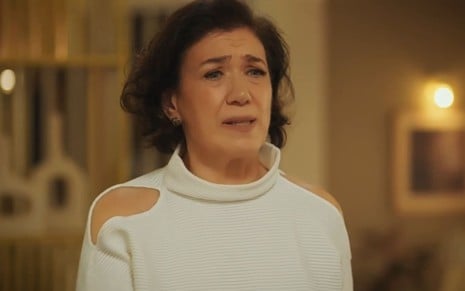 Lilia Cabral caracterizada como Bebel; ela usa uma blusa branca em cena de Fuzuê; atriz exprime preocupação.
