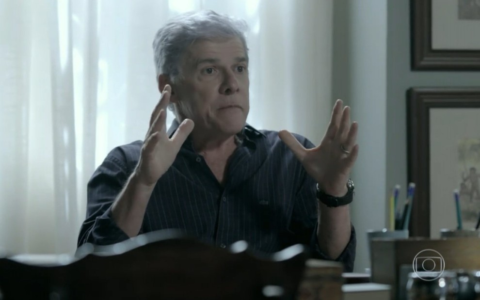 Cláudio (José Mayer) está sentado em escritório e gesticula com a mão em cena de Império
